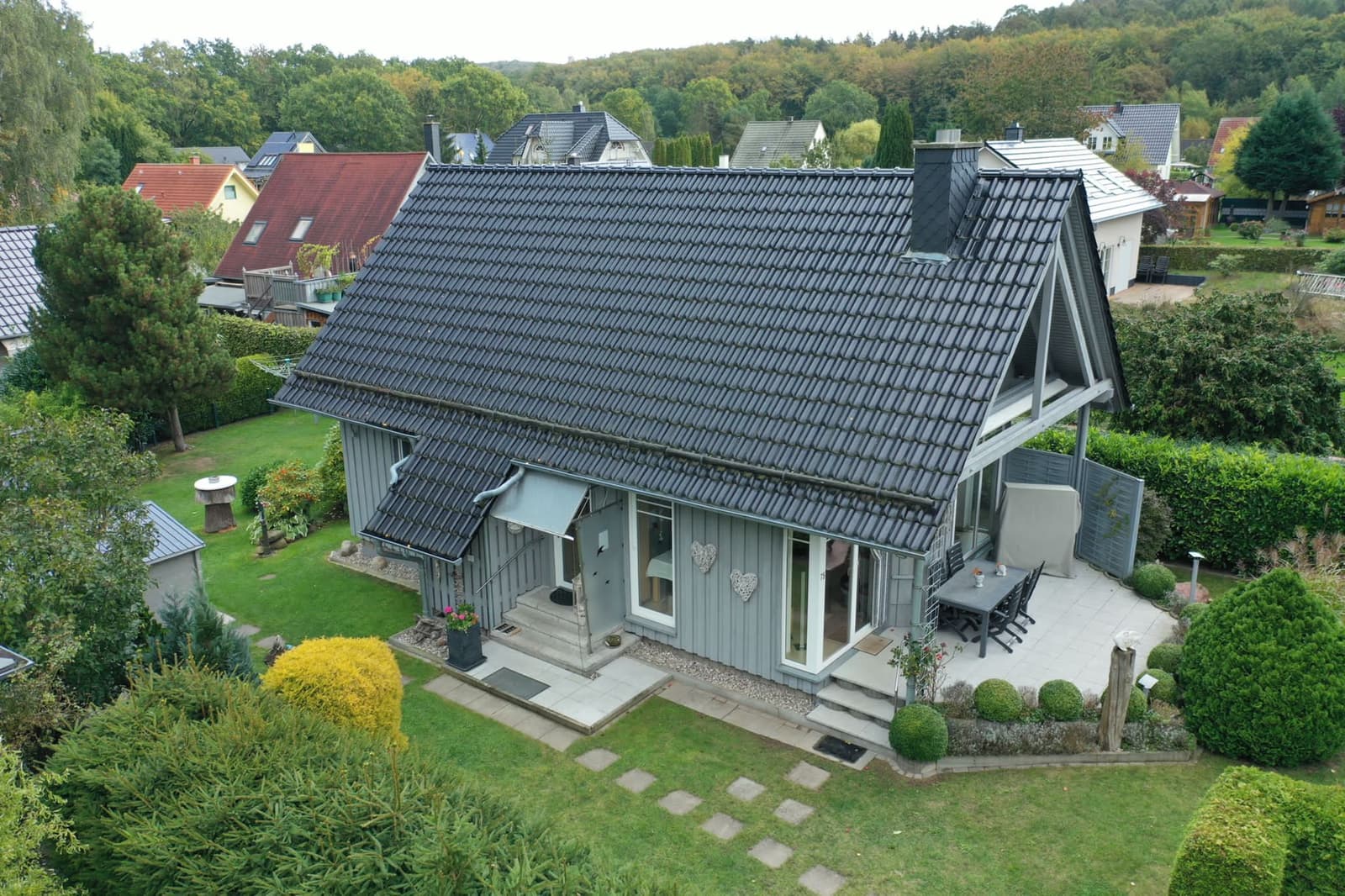 Luftaufnahme des Ferienhauses mit Garten, dahinter bewaldete Hügel