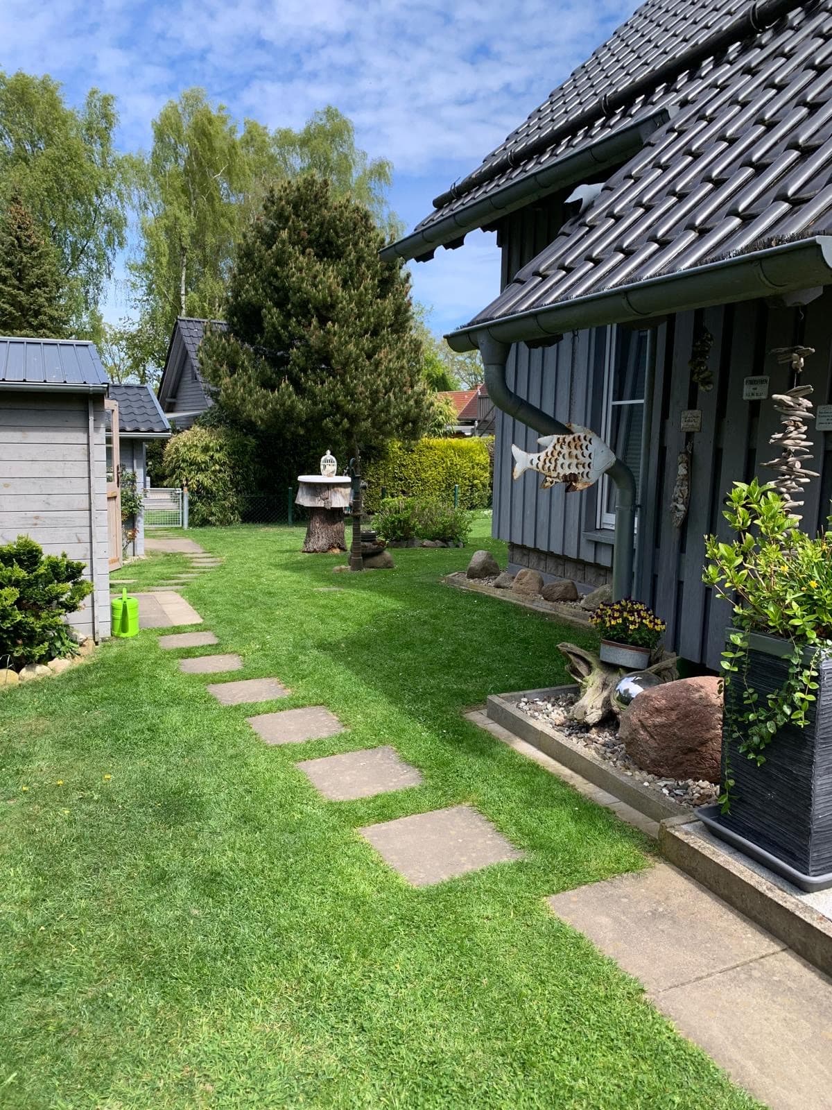 Trittsteinweg am Haus entlang zum Gartenhaus, in der Mitte ein Vogelhäuschen