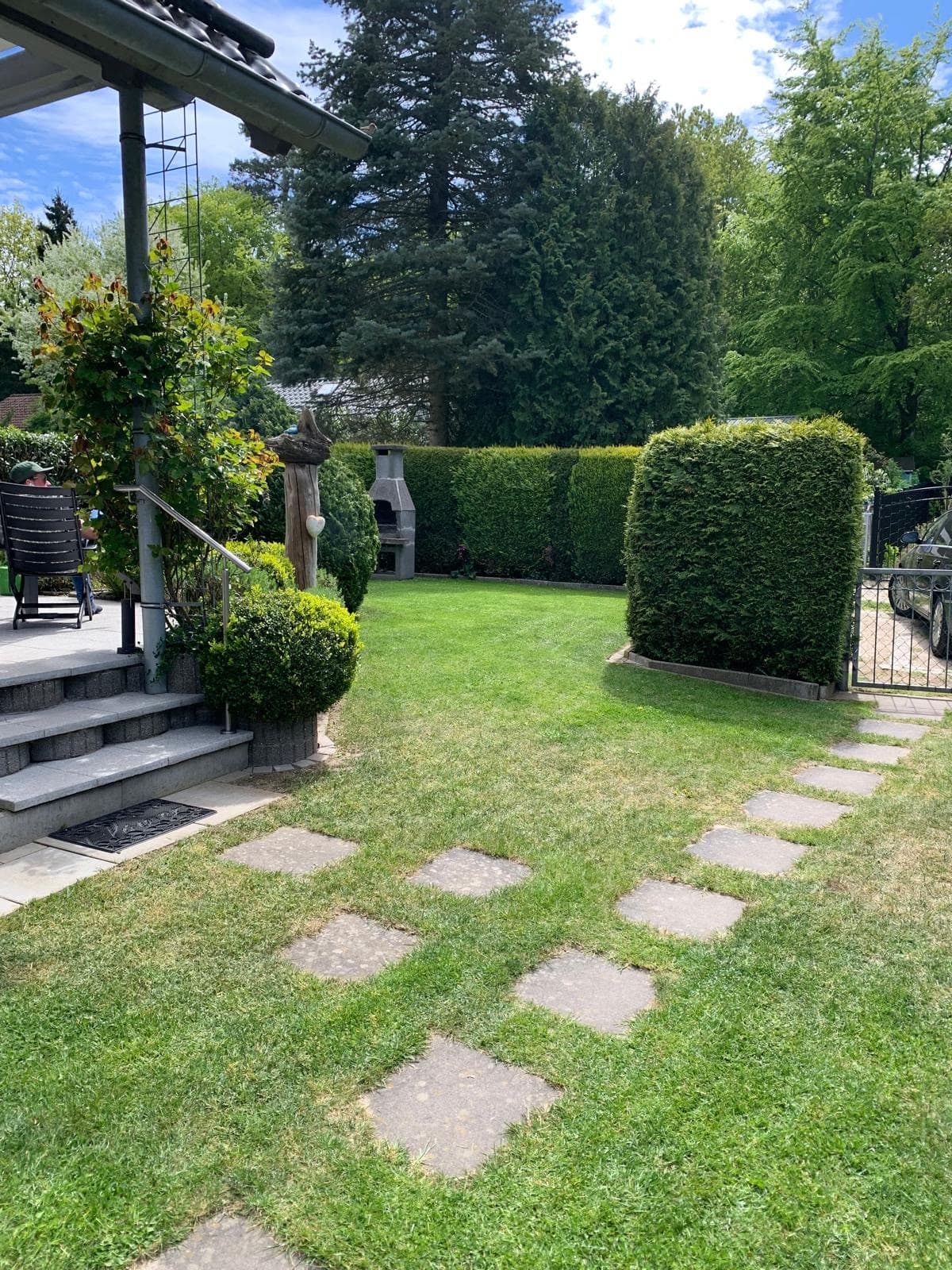Trittsteine über den Rasen zu den Terrassenstufen, rechts das Gartentor, dahinter parkt ein Auto